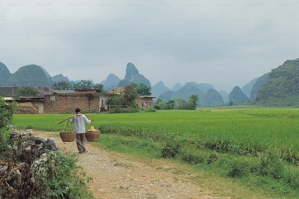 a man walking down a dirt road carrying a basket