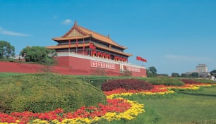 a large building with a red roof surrounded by yellow and red flowers