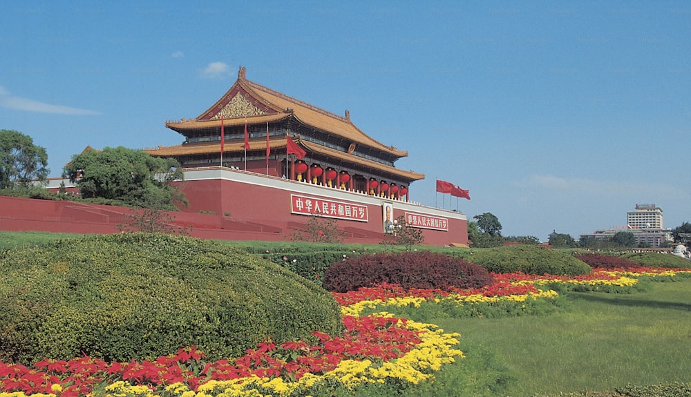 a large building with a red roof surrounded by yellow and red flowers