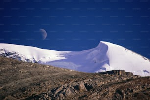 the moon is setting over a snowy mountain