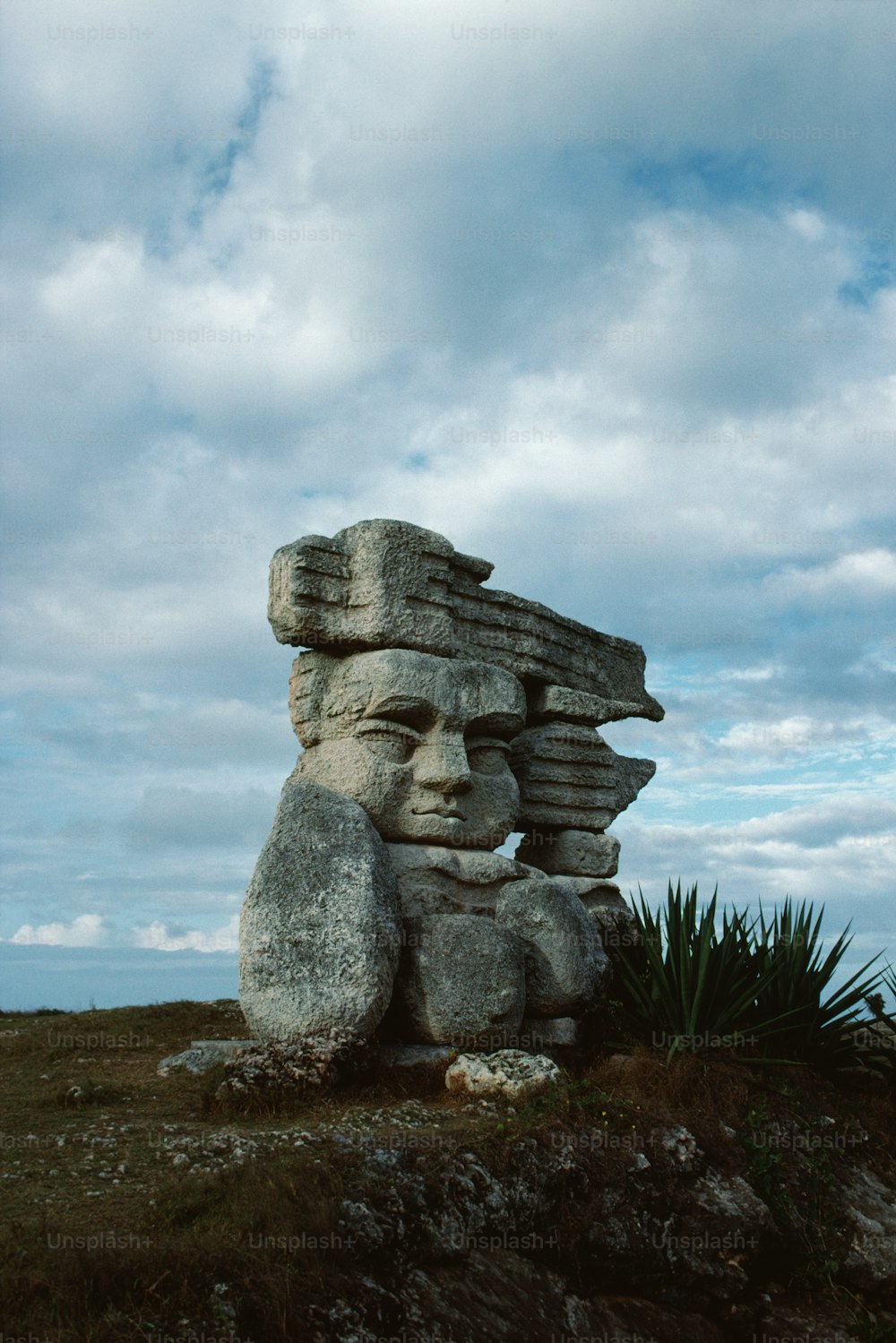 une grande statue de pierre assise au sommet d’un champ verdoyant