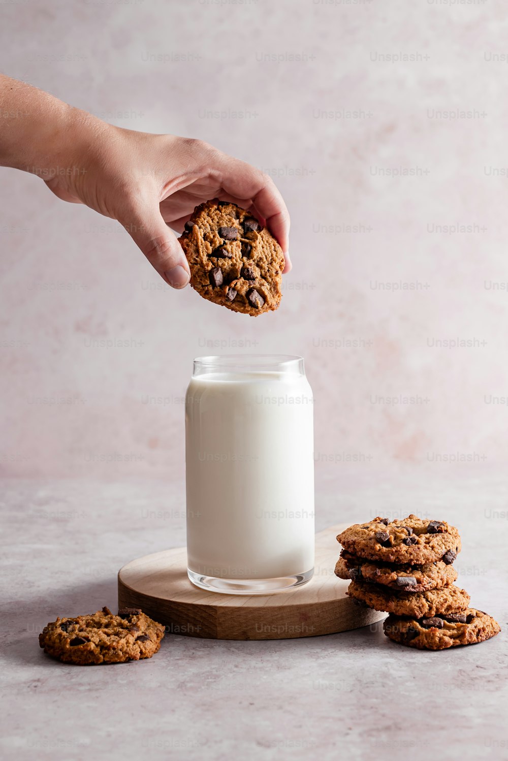 a person holding a cookie over a glass of milk