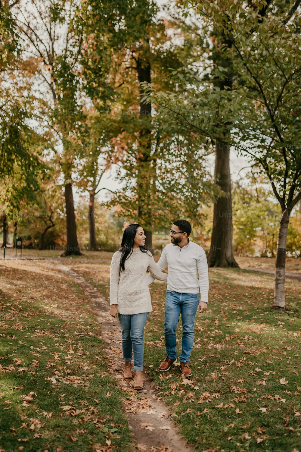 a man and woman walking through a park holding hands