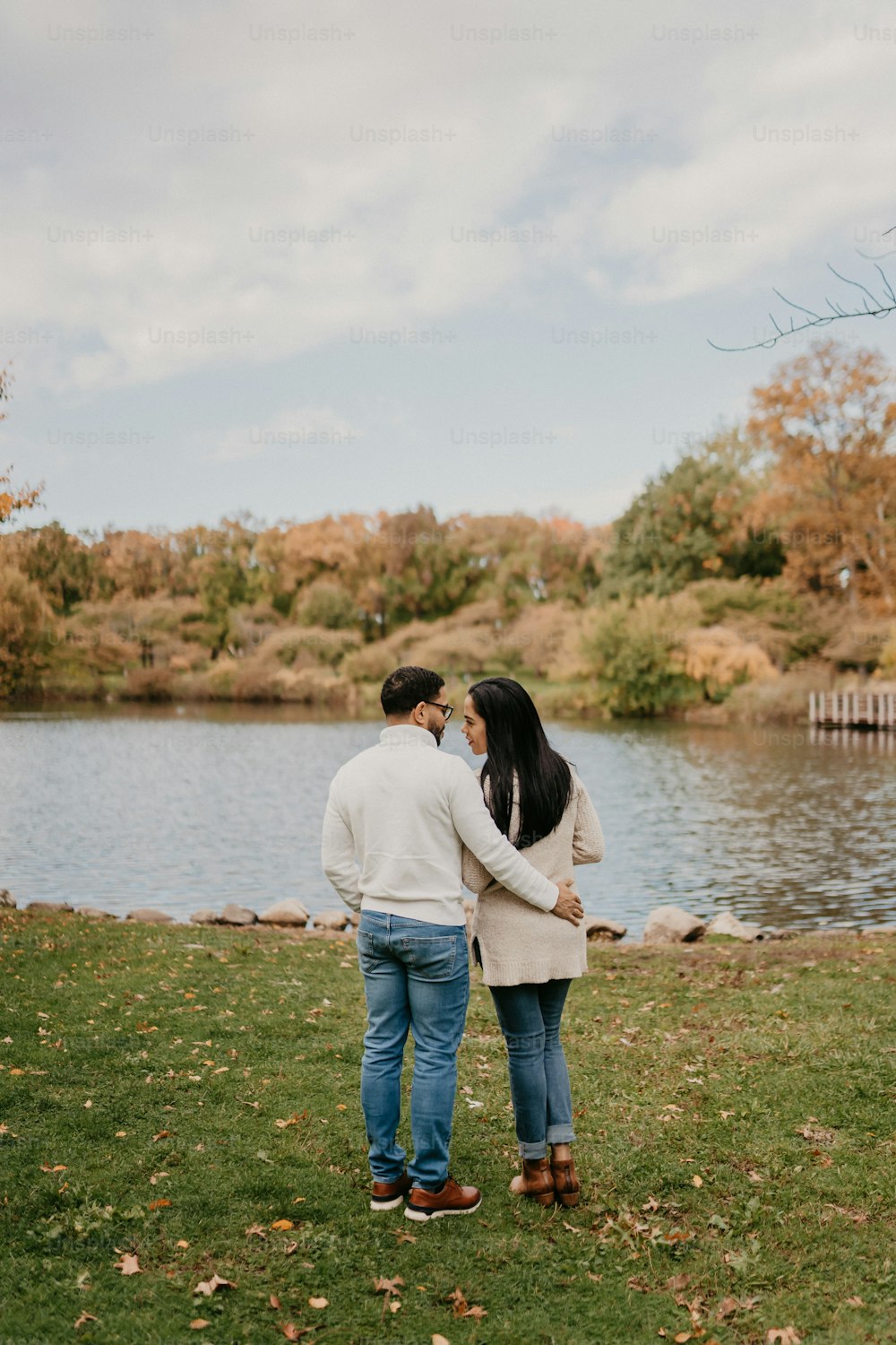 a man and a woman standing next to each other in front of a lake