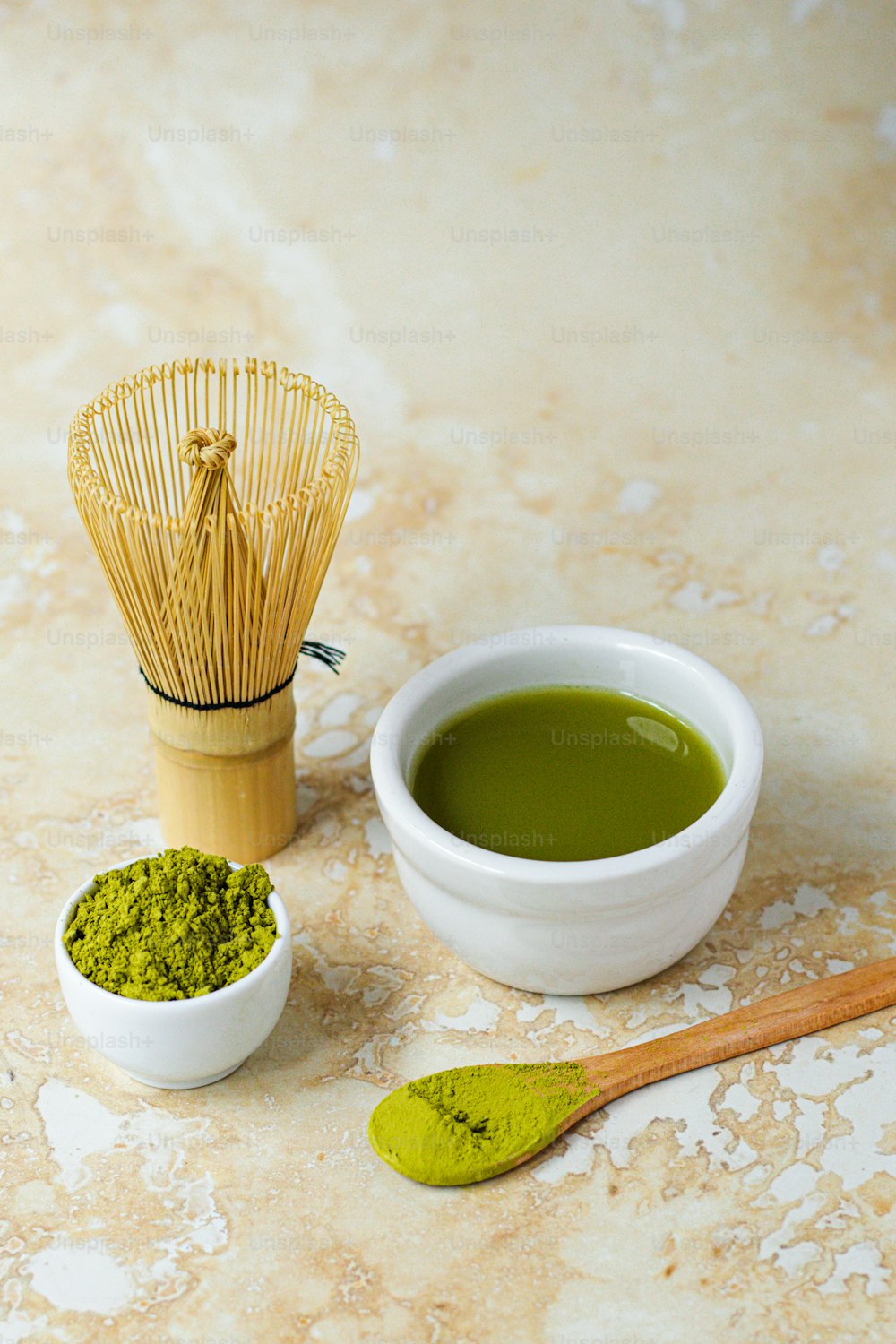 a bowl of green tea next to a whisk and spoon
