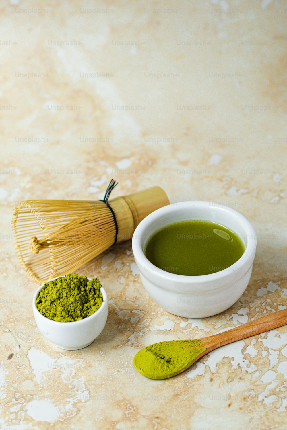 un tazón de té verde junto a un batidor y una cuchara