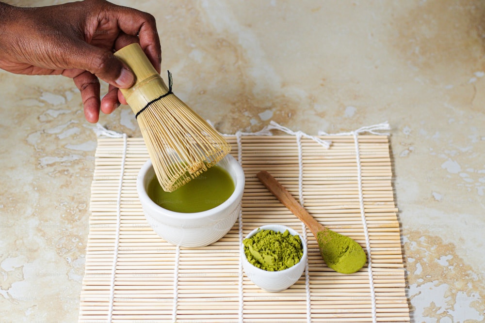 a person holding a wooden brush over a cup of green tea