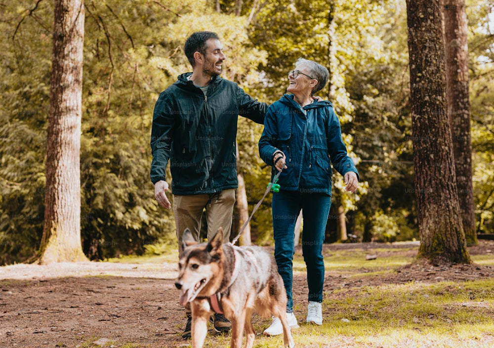 um homem e uma mulher passeando com um cachorro por uma floresta