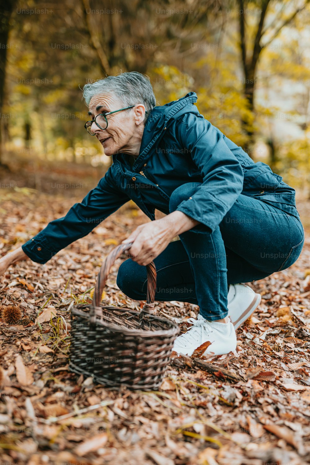 an older woman picking up leaves from a basket