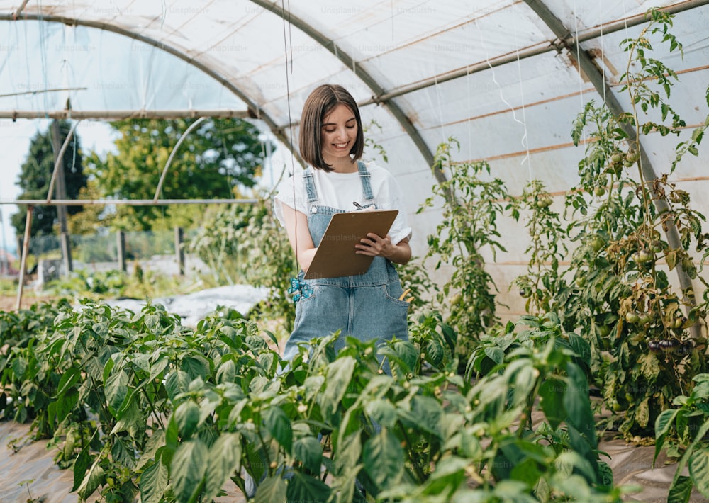 a woman standing in a greenhouse holding a clipboard