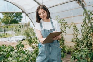 a woman standing in a greenhouse holding a clipboard