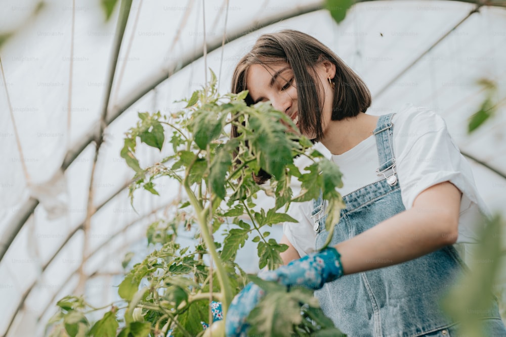 a woman in overalls tending to plants in a greenhouse