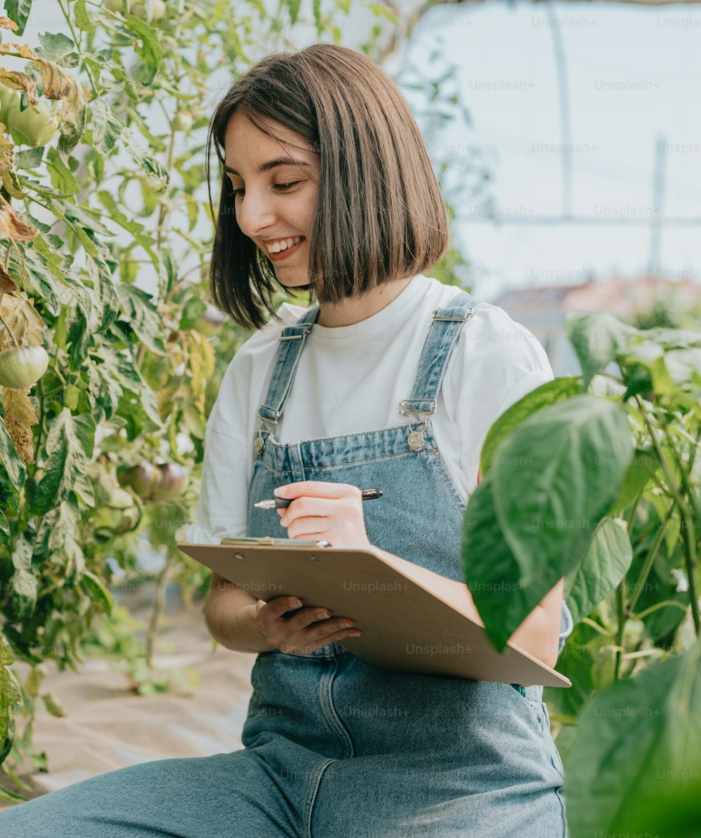 a woman in overalls holding a clipboard in a greenhouse