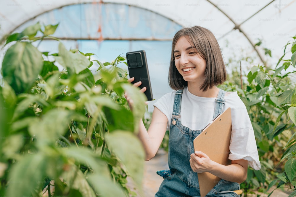 Una mujer en overol sosteniendo un teléfono celular en un invernadero