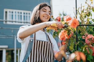 a woman in a striped apron trimming a bush of flowers