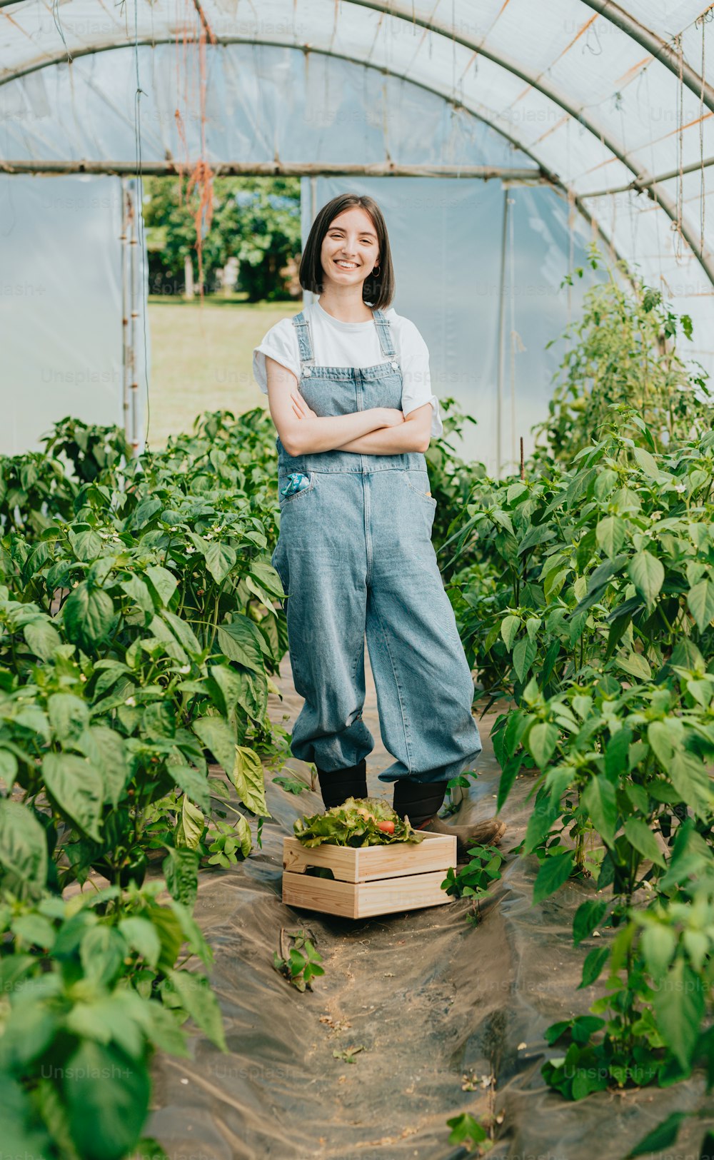 a woman standing in a greenhouse with her arms crossed