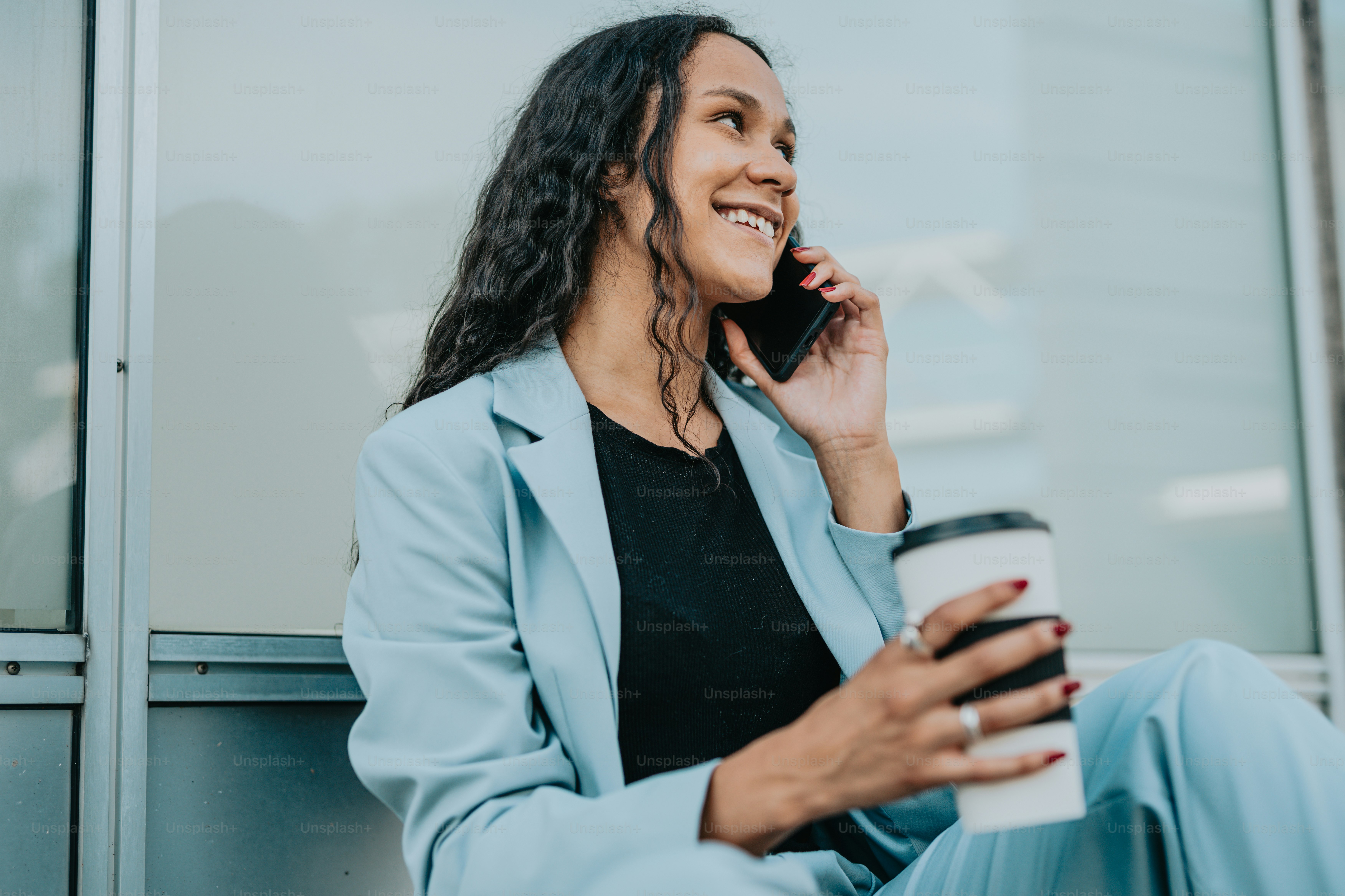 a woman talking on a cell phone while holding a cup of coffee