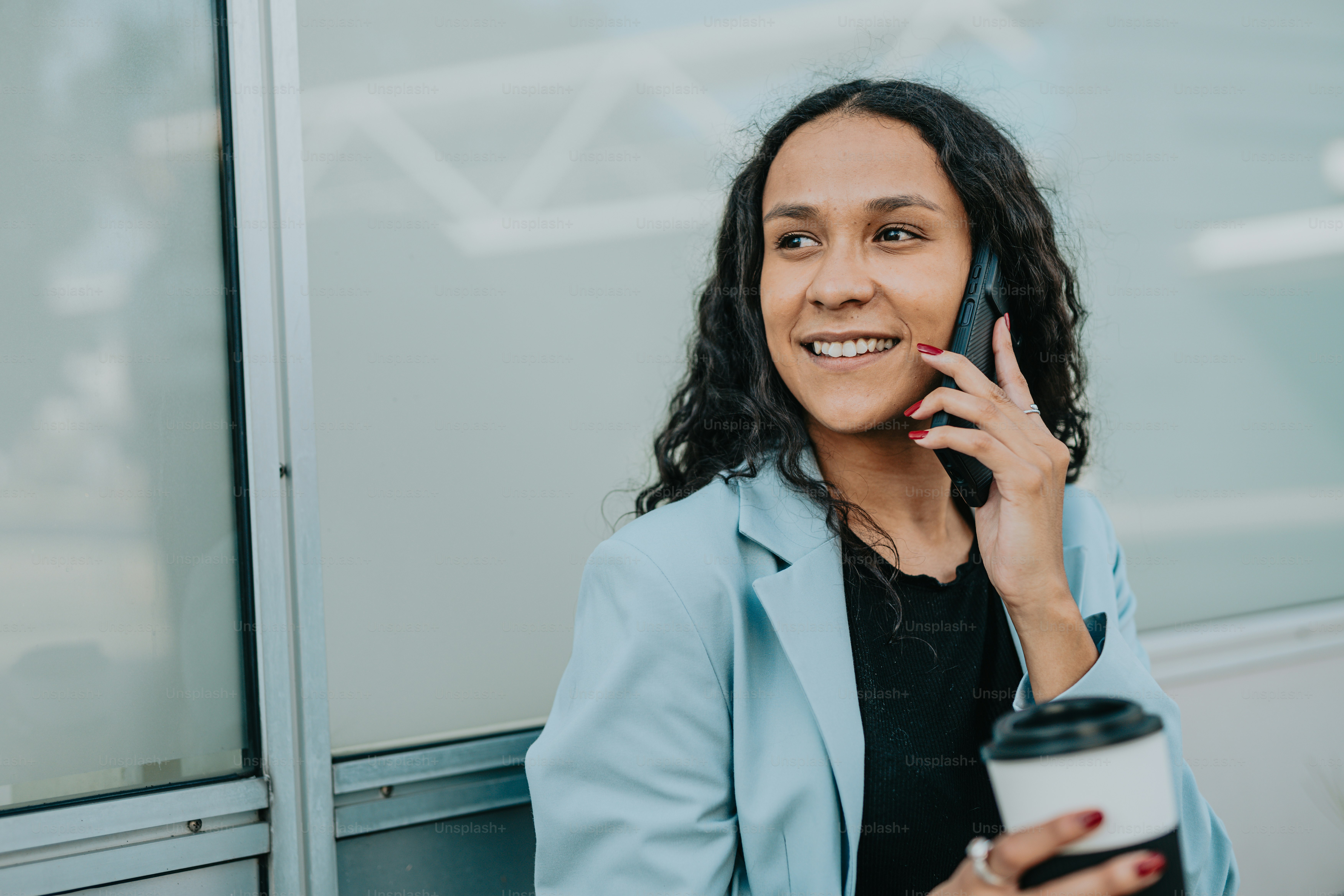 uma mulher falando ao celular enquanto segura uma xícara de café