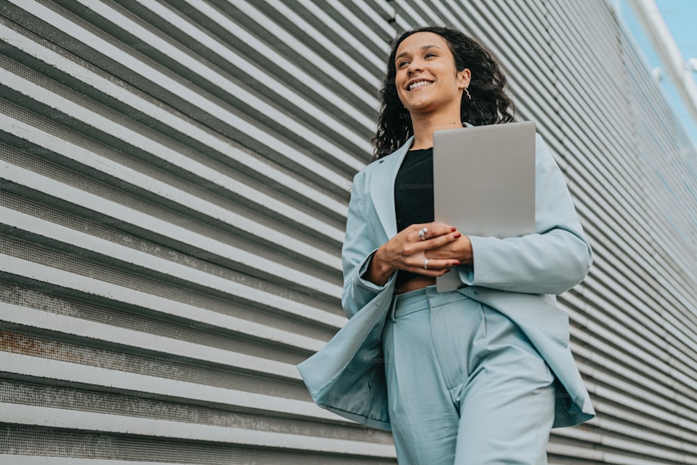 a woman standing in front of a building holding a laptop