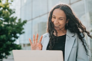 Una mujer con cabello largo sonriendo y levantando la mano frente a una computadora portátil