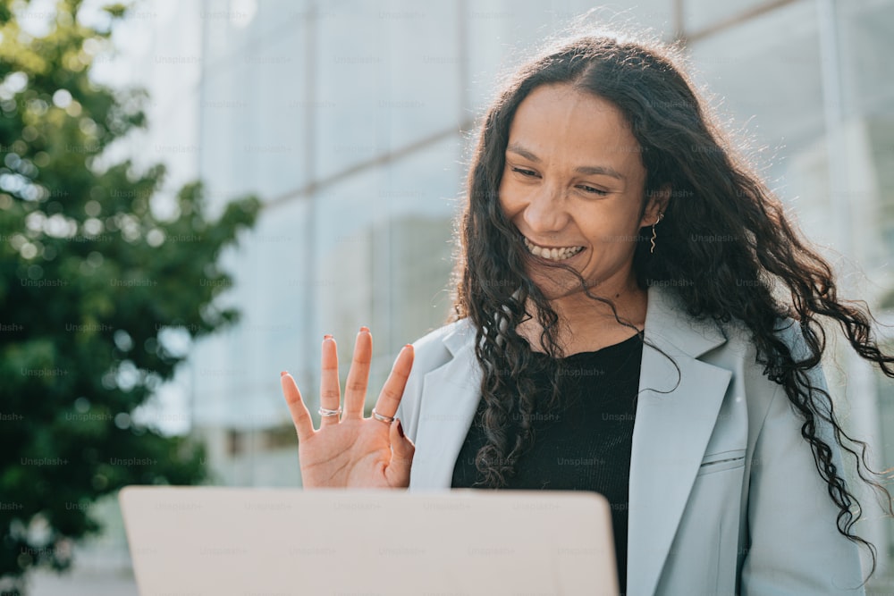 a woman with long hair smiling and holding her hand up in front of a laptop