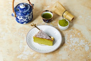 a piece of cake on a plate next to a cup of green tea