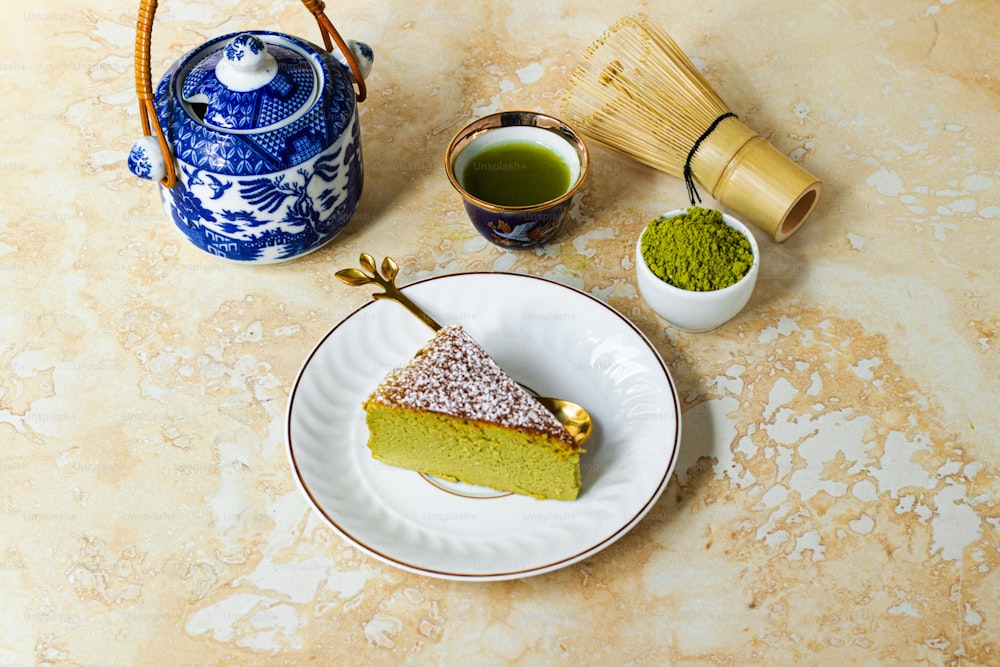 a piece of cake on a plate next to a cup of green tea