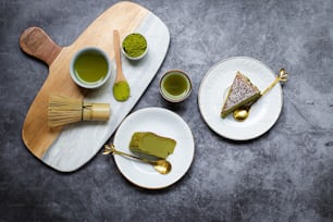 a plate with a piece of cake and two cups of green tea