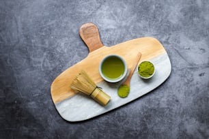 una taza de té verde junto a una cuchara de madera y batidora