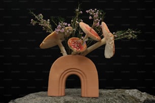 a vase filled with flowers and mushrooms on top of a rock