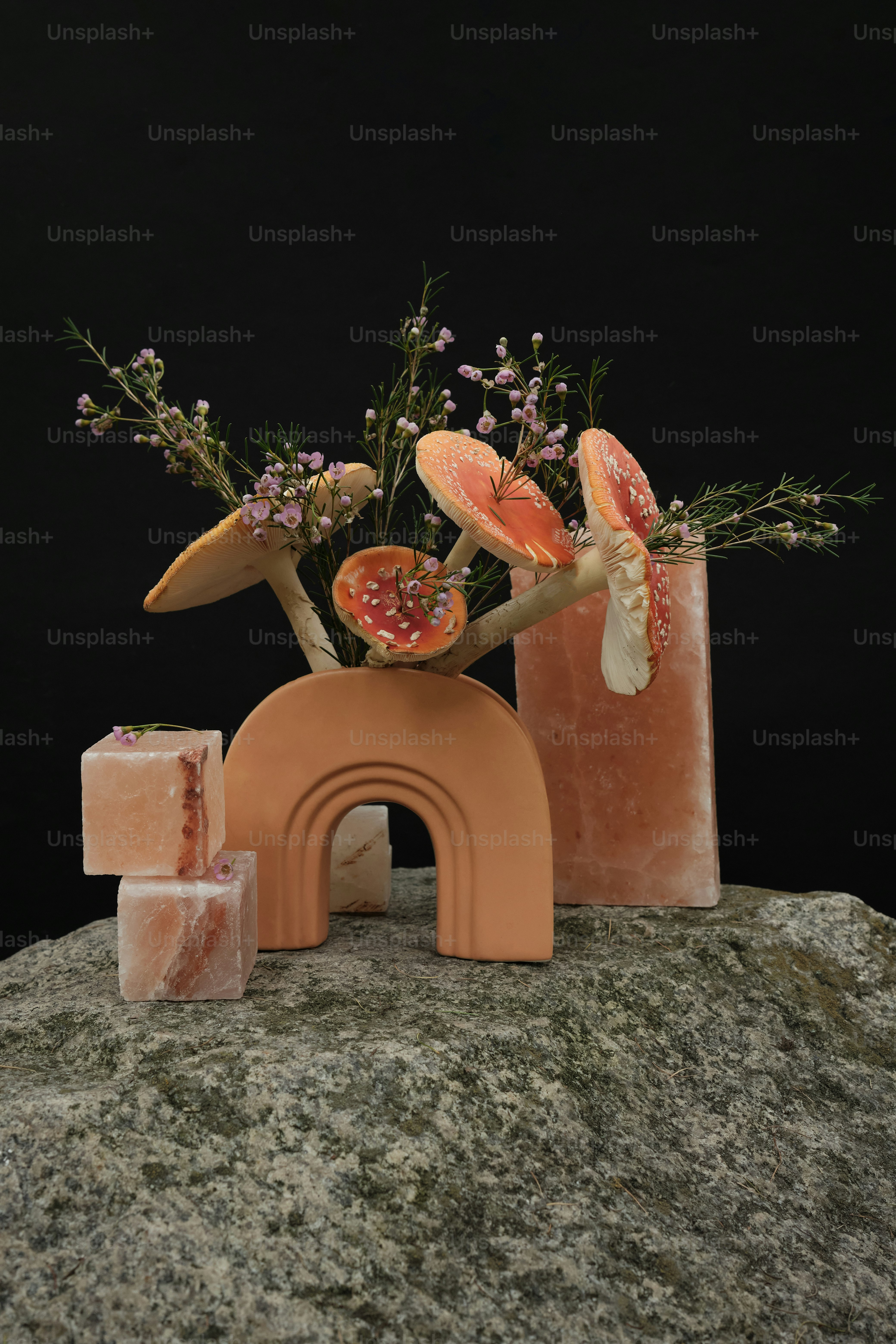 a vase with flowers and fruit on top of a rock