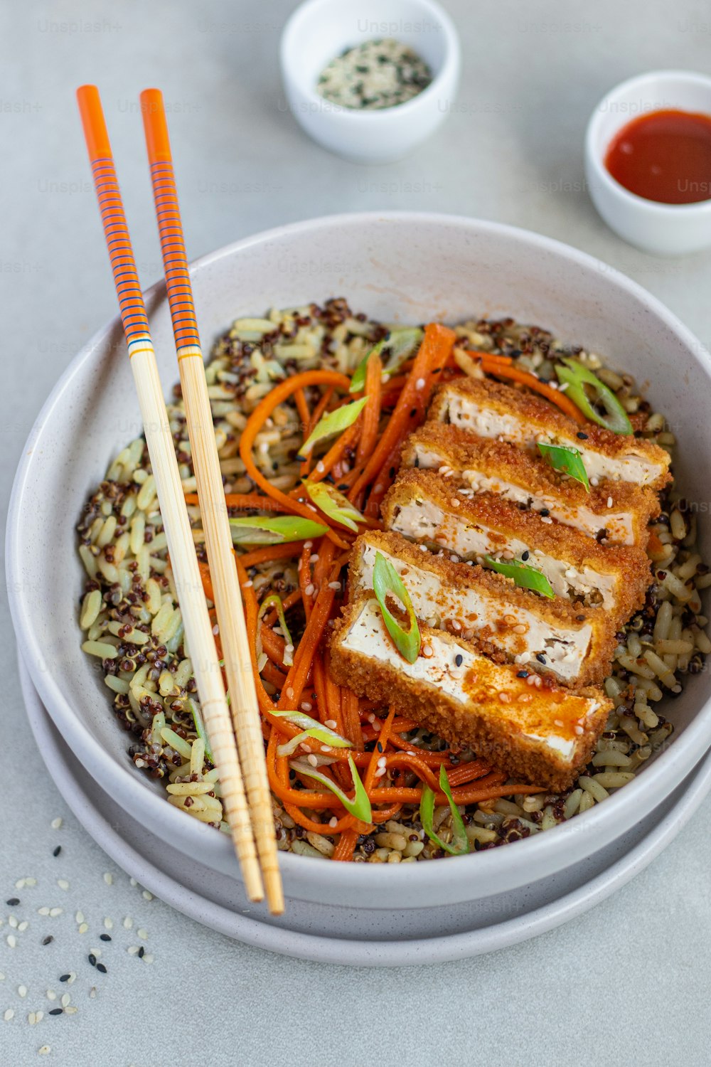 a bowl of food with carrots, rice and chopsticks