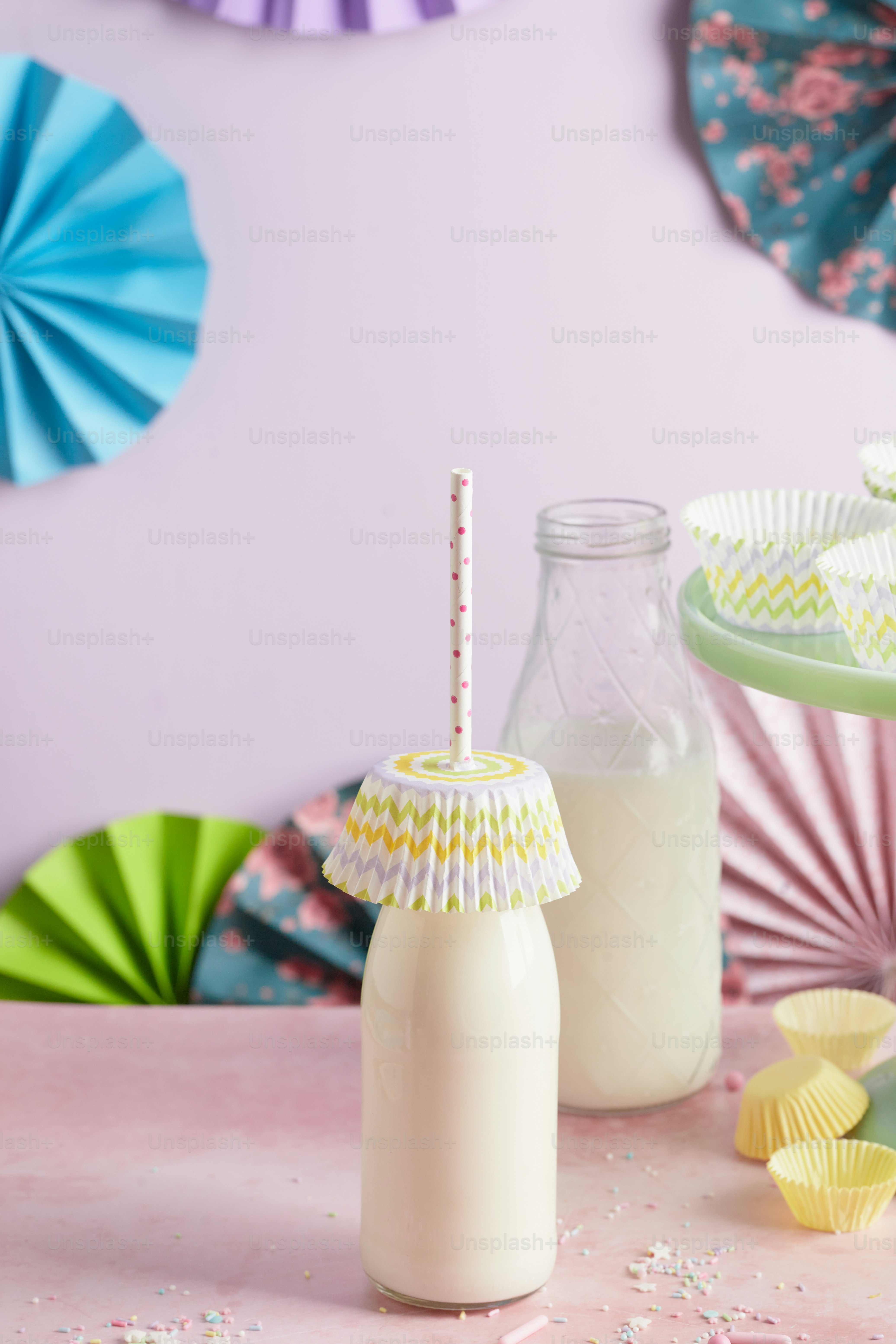 a table topped with a bottle of milk next to a plate of cupcakes