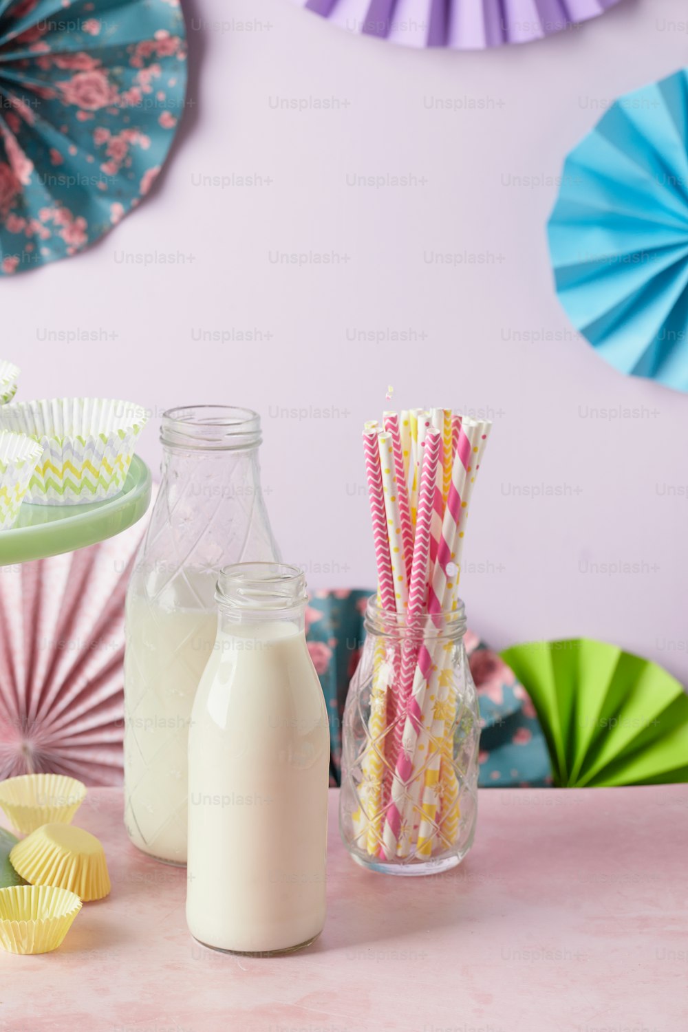 a pink table topped with a bottle of milk and paper fans
