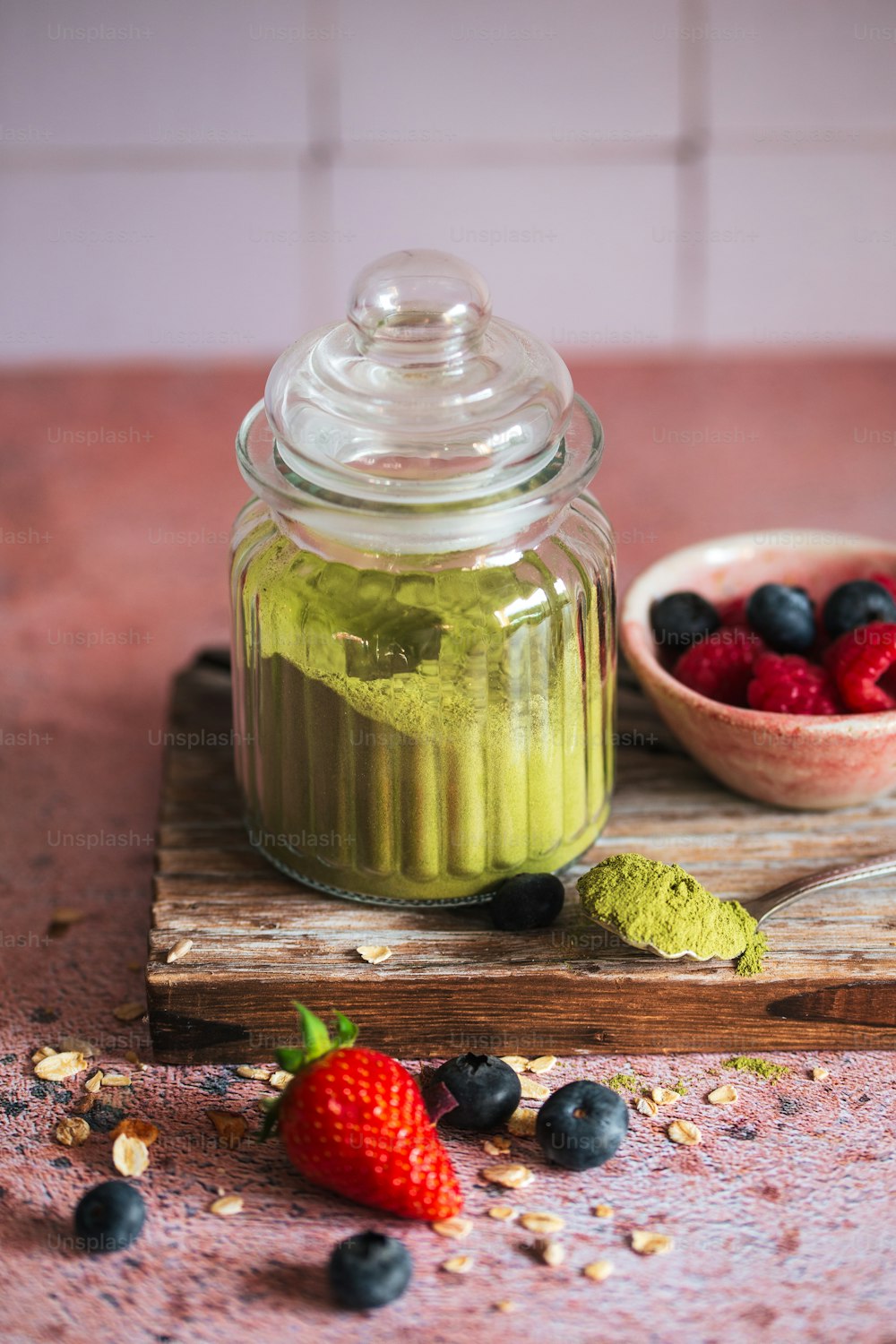 a glass jar filled with green liquid next to a bowl of berries