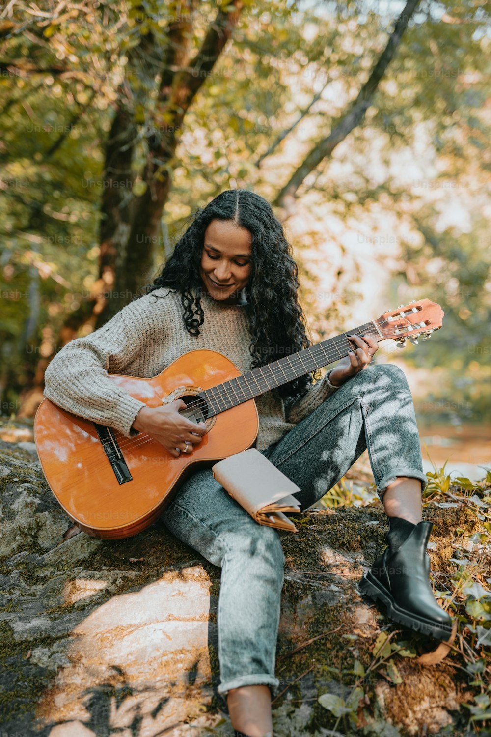 a woman sitting on a rock playing a guitar