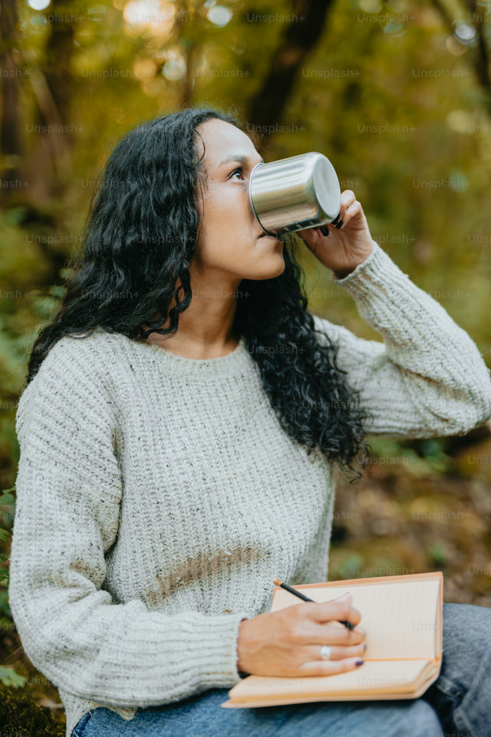 Una mujer sentada en el bosque bebiendo de una taza