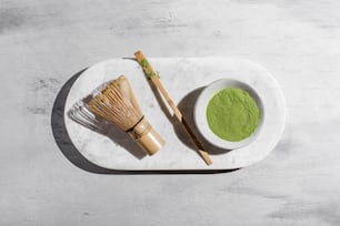 a white plate topped with a bowl of green powder next to a whisk