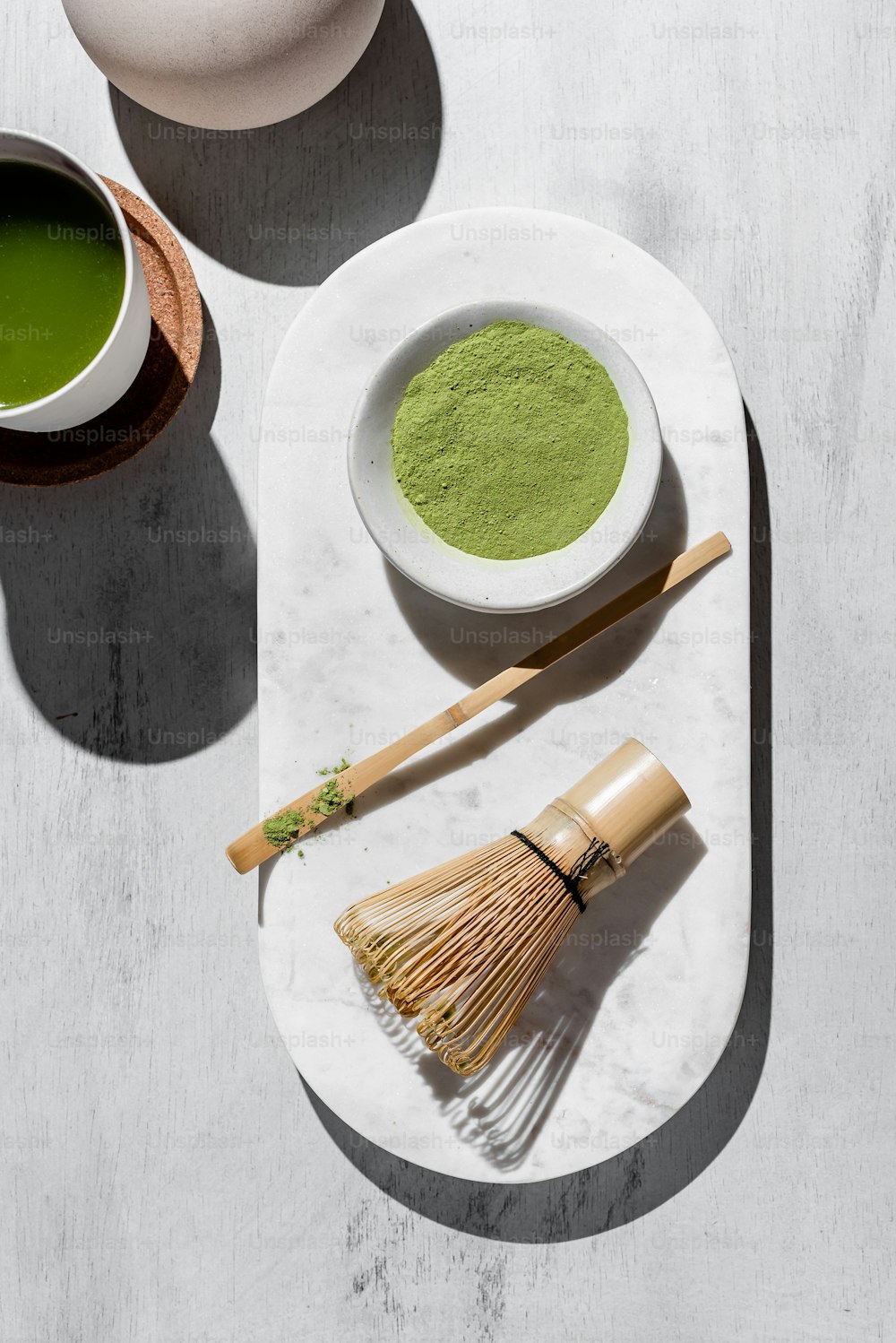 a white plate topped with a bowl of green tea next to a whisk