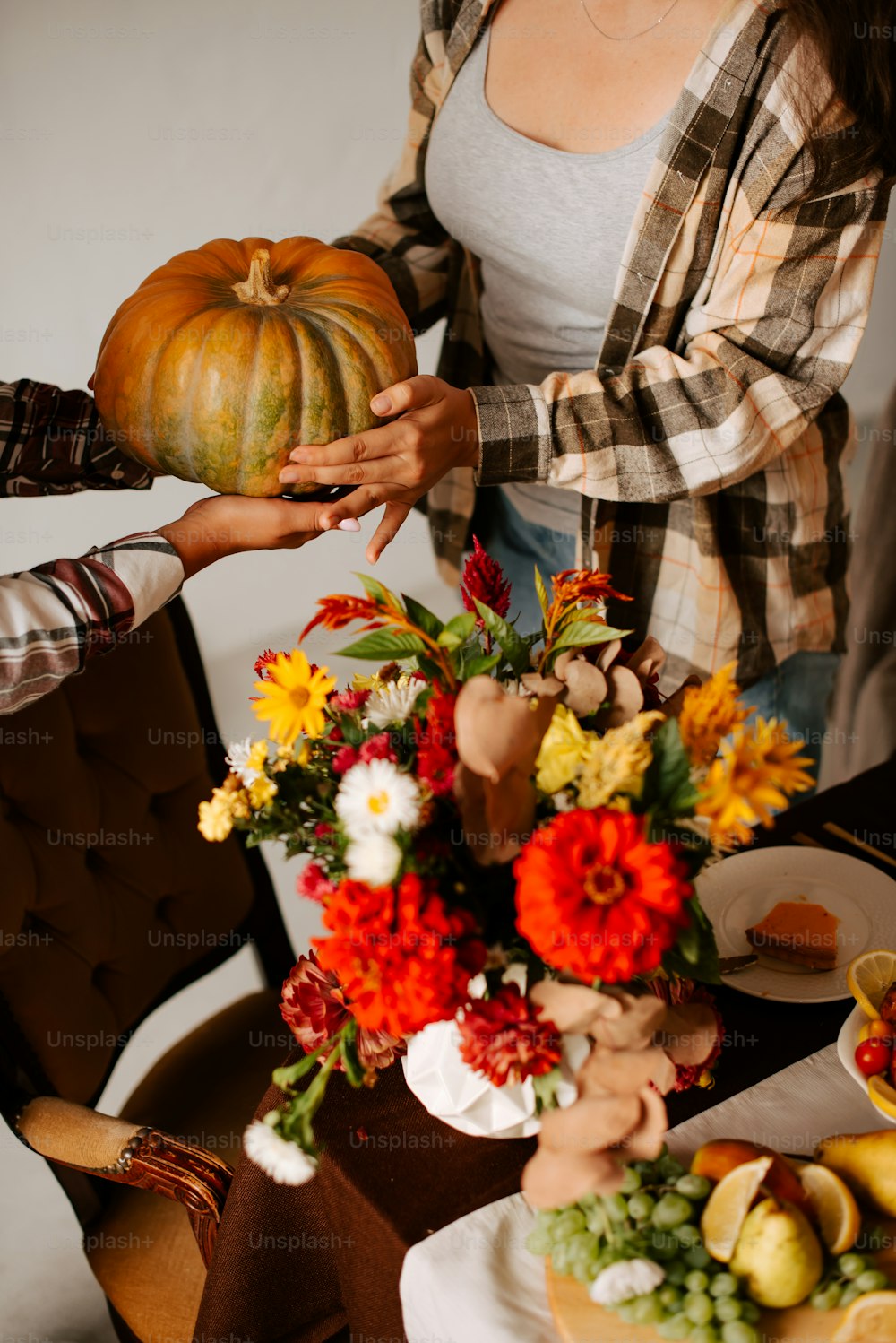 a woman holding a pumpkin over a table filled with flowers