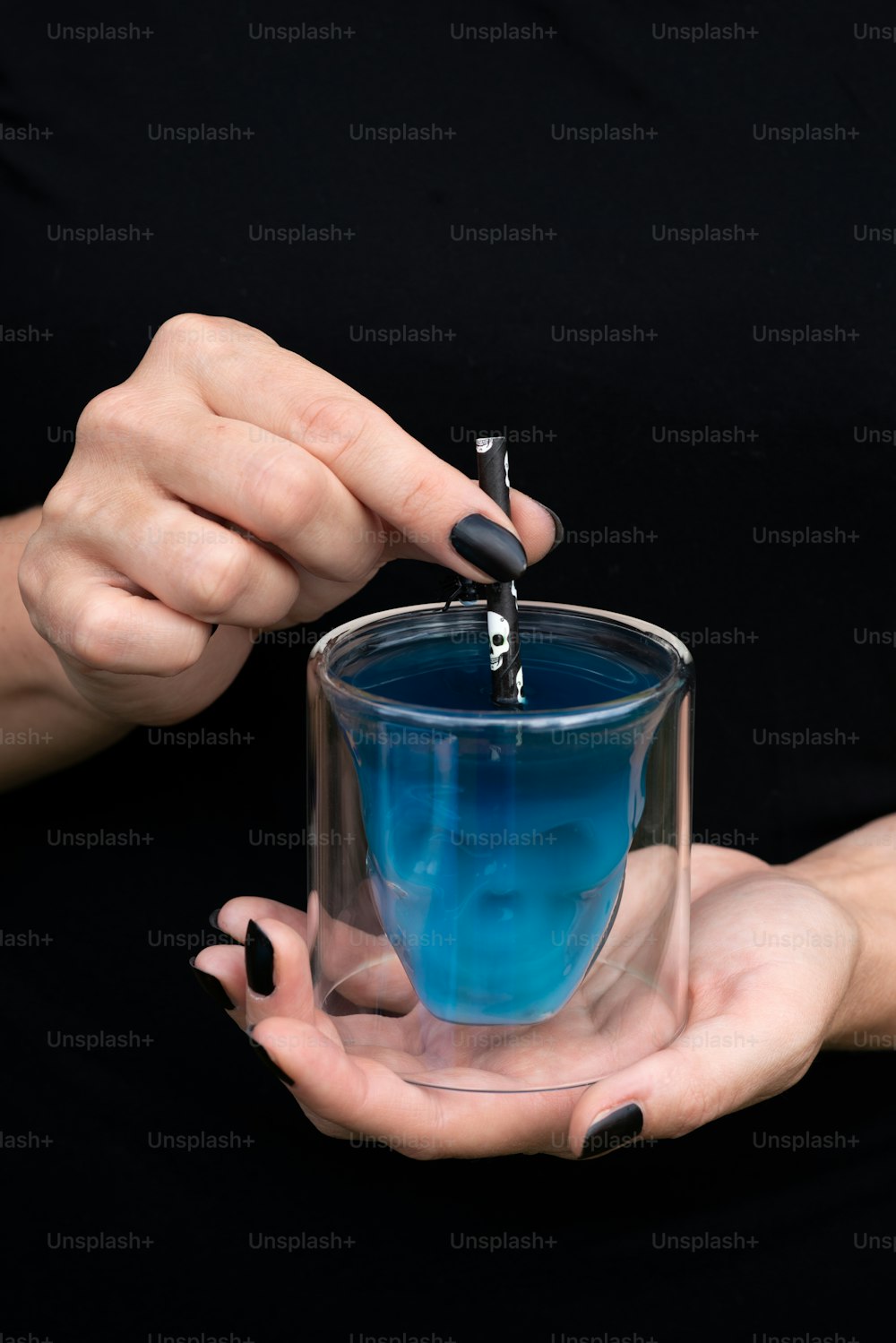 a woman is holding a glass with blue liquid in it