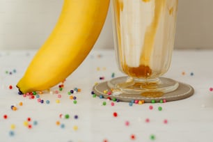 uma banana sentada ao lado de um copo cheio de líquido e polvilha;