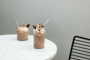 two glasses of chocolate milkshakes sitting on a table