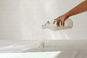 eine person gießt milch in ein glas