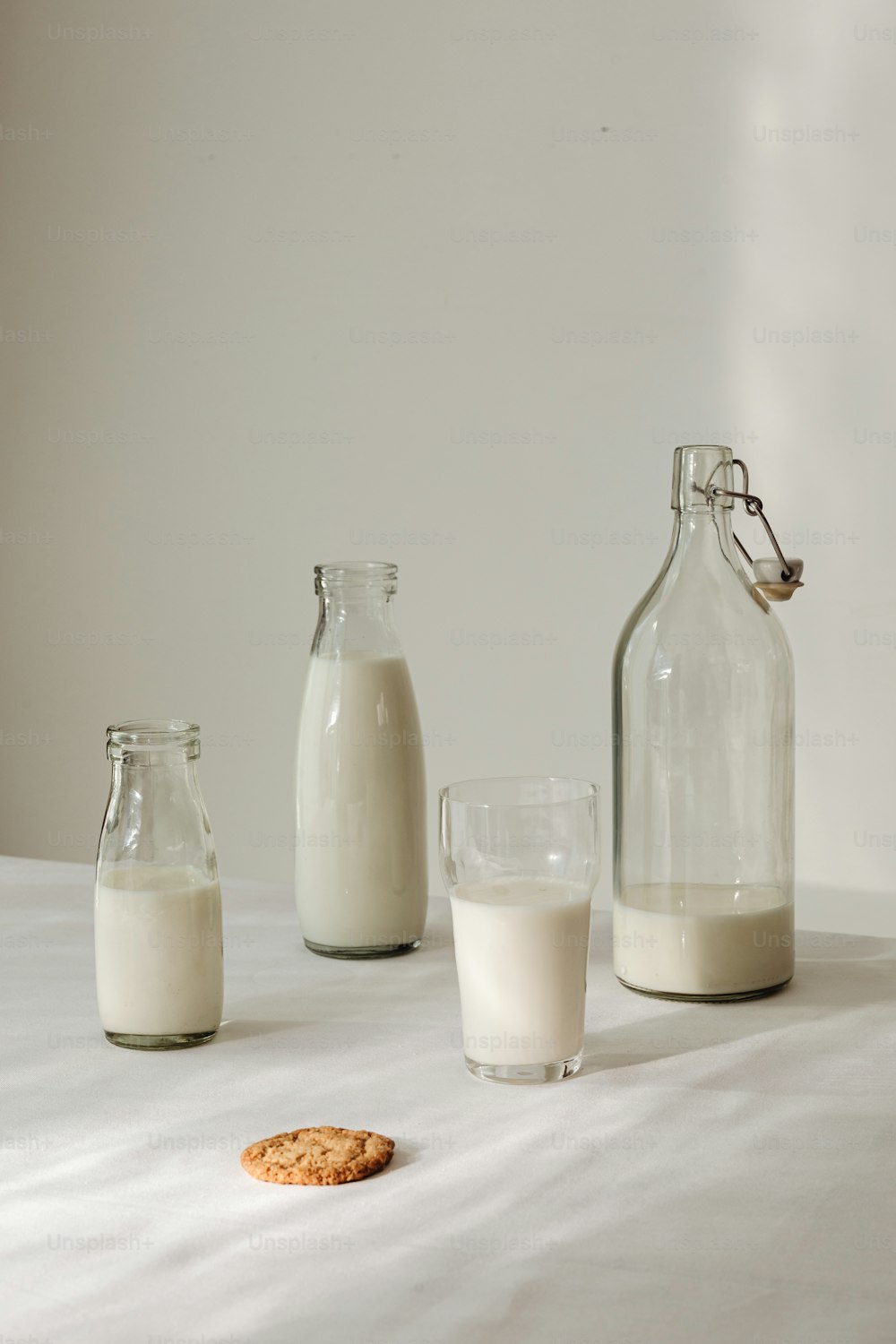 ein Glas Milch, eine Flasche Milch und ein Keks auf einem Tisch