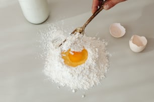 uma pessoa segurando um batedor sobre uma pilha de farinha e ovos