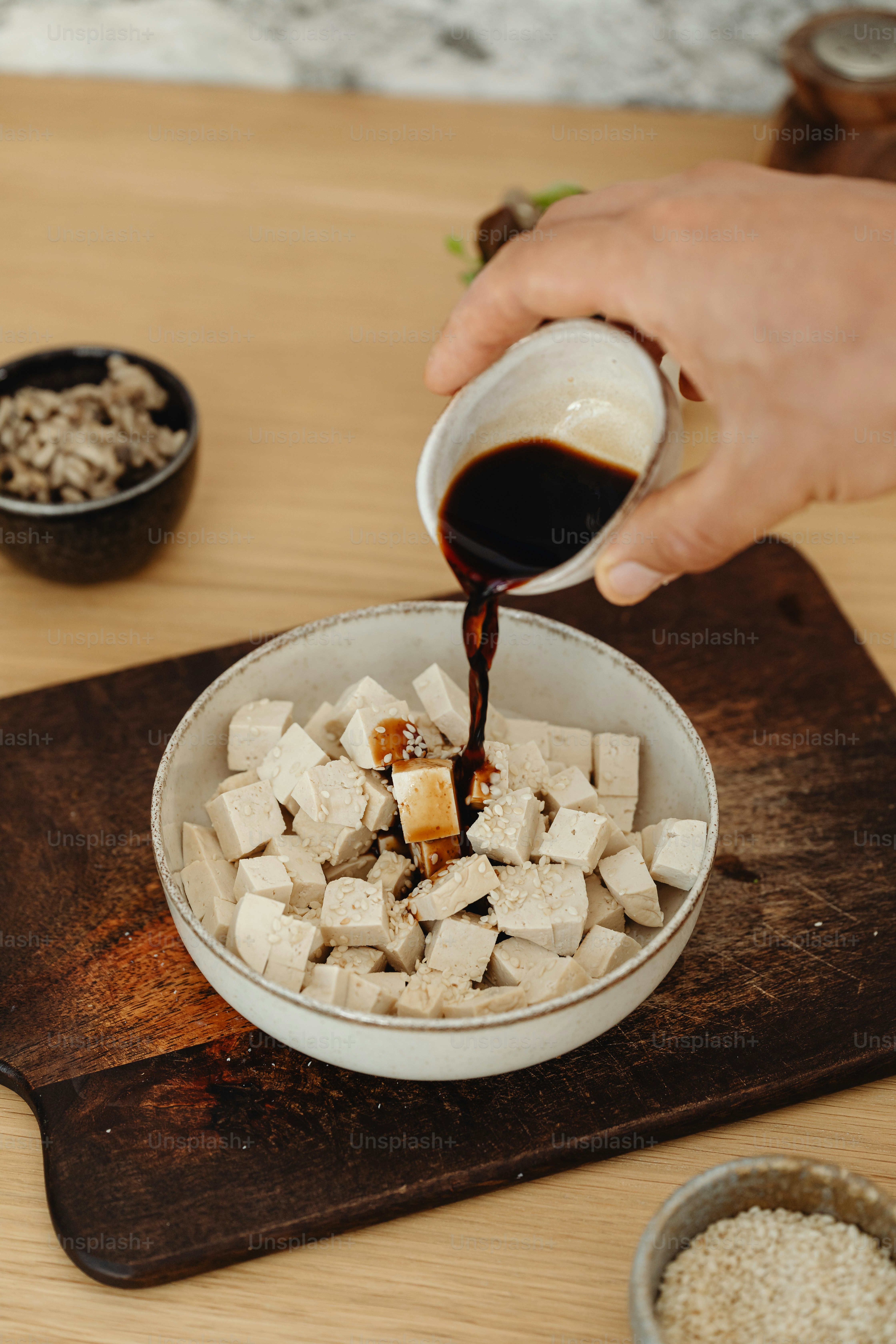 a person pouring sauce into a bowl of tofu