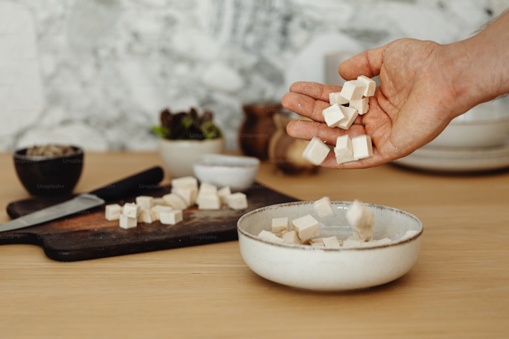 a person's hand holding a handful of sugar over a bowl of sugar cube