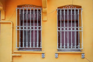 a yellow building with two windows and bars