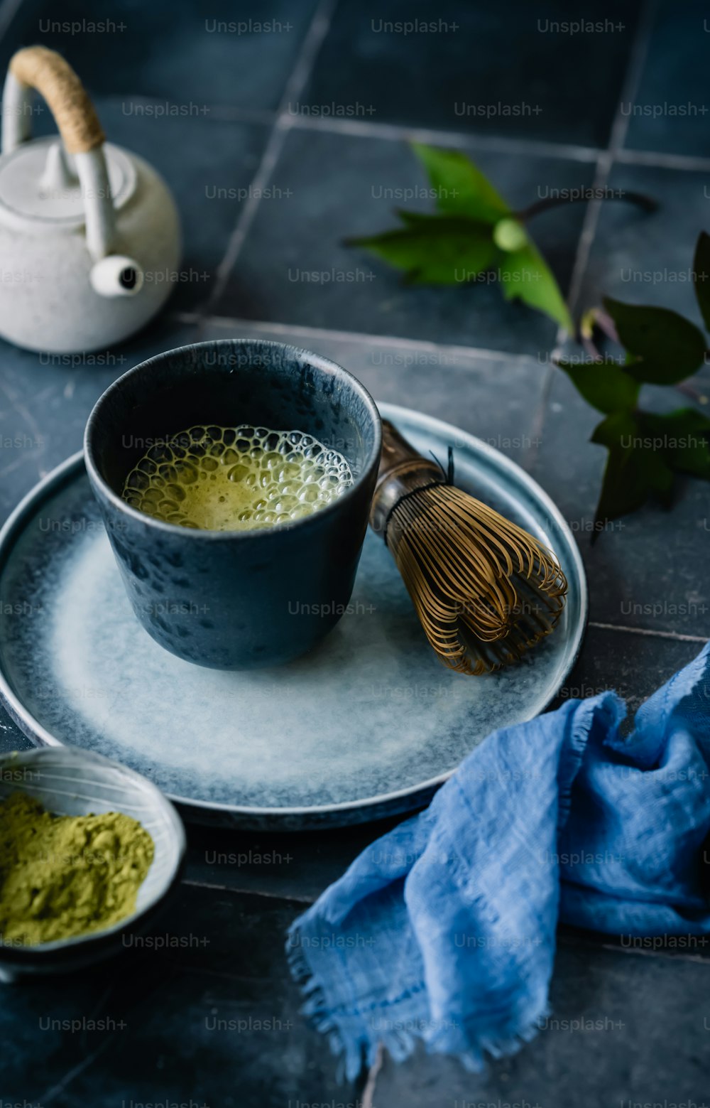 a bowl of green tea next to a whisk on a plate